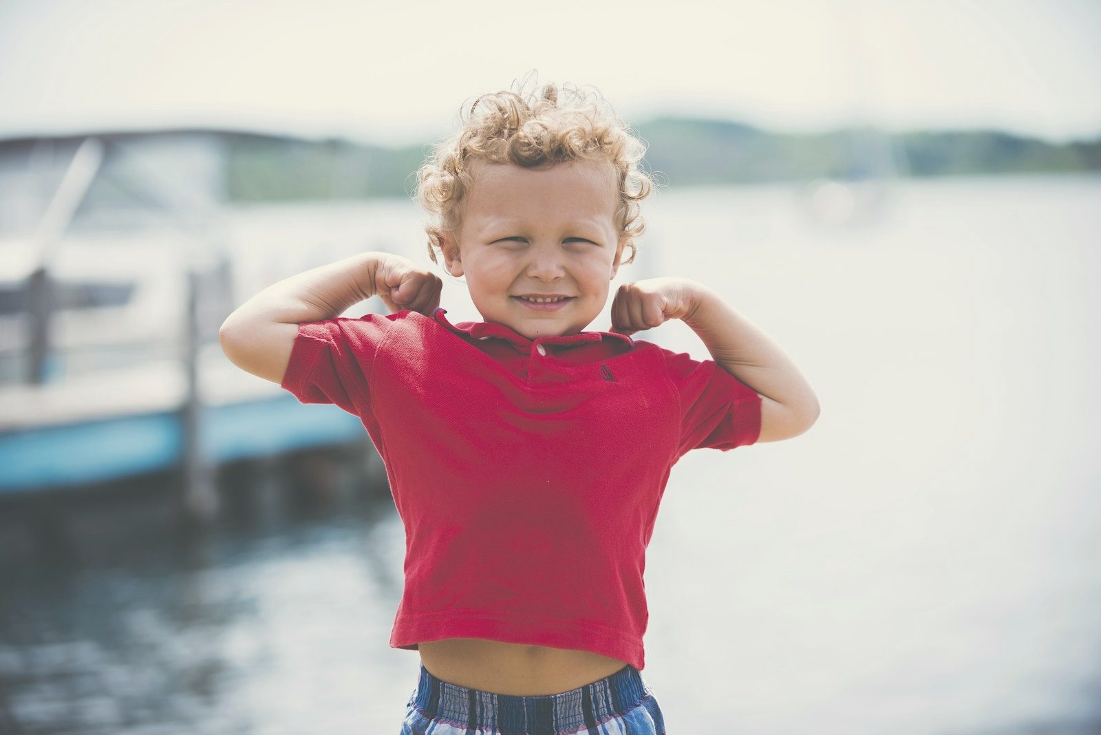 A young boy in a red shirt outdoors, hands behind his head