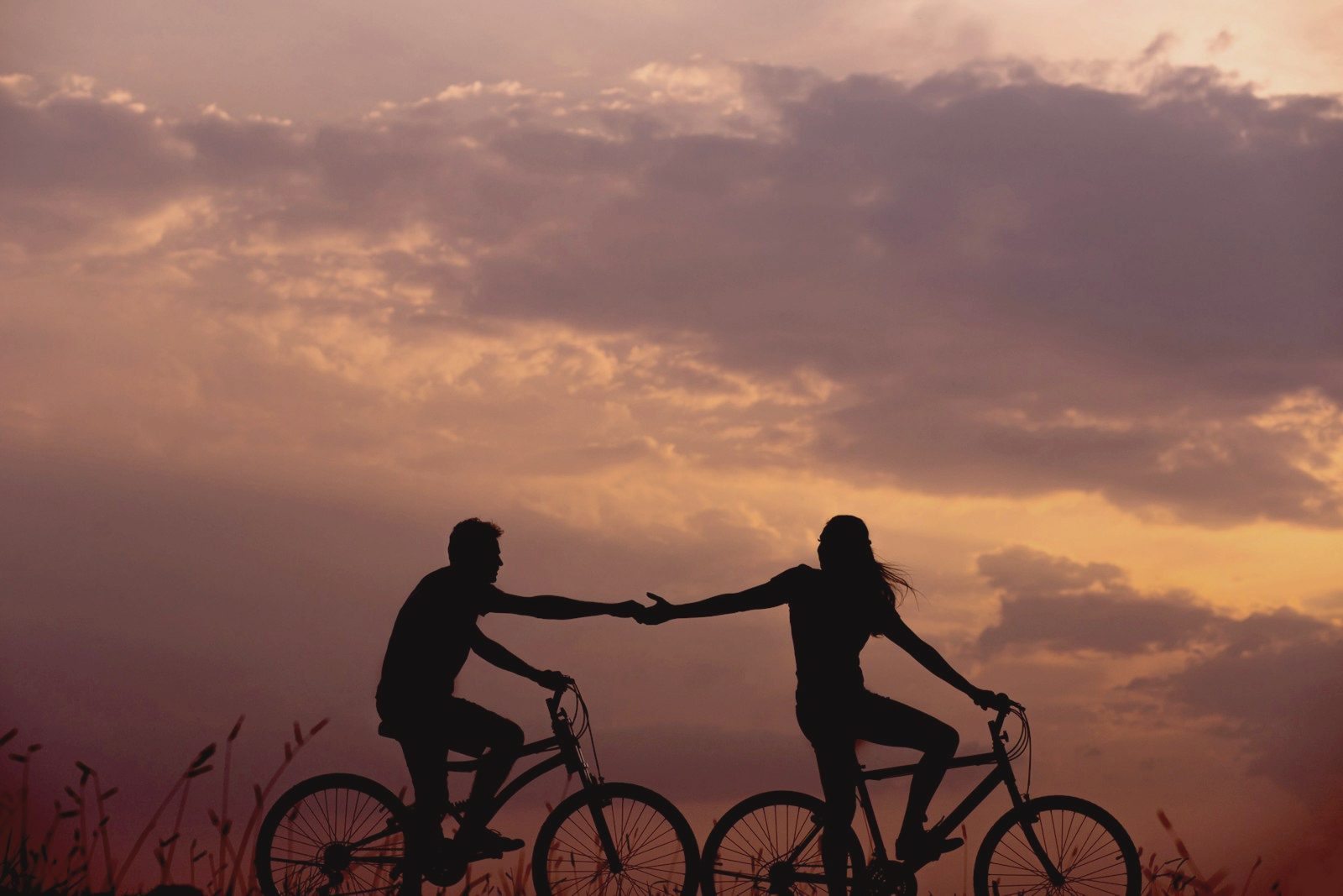 Two cyclists reaching for each other's hand at sunset