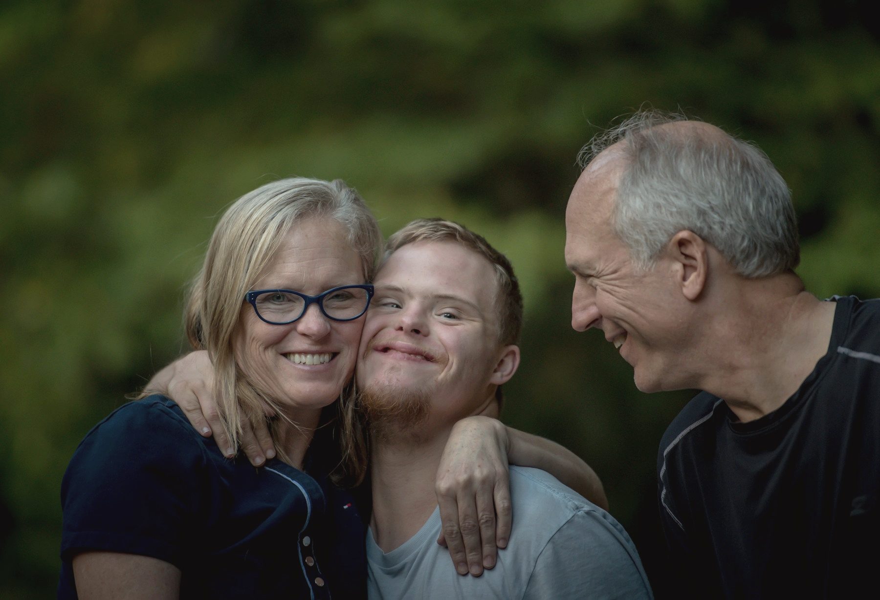 Three family members leaning in close together, smiling