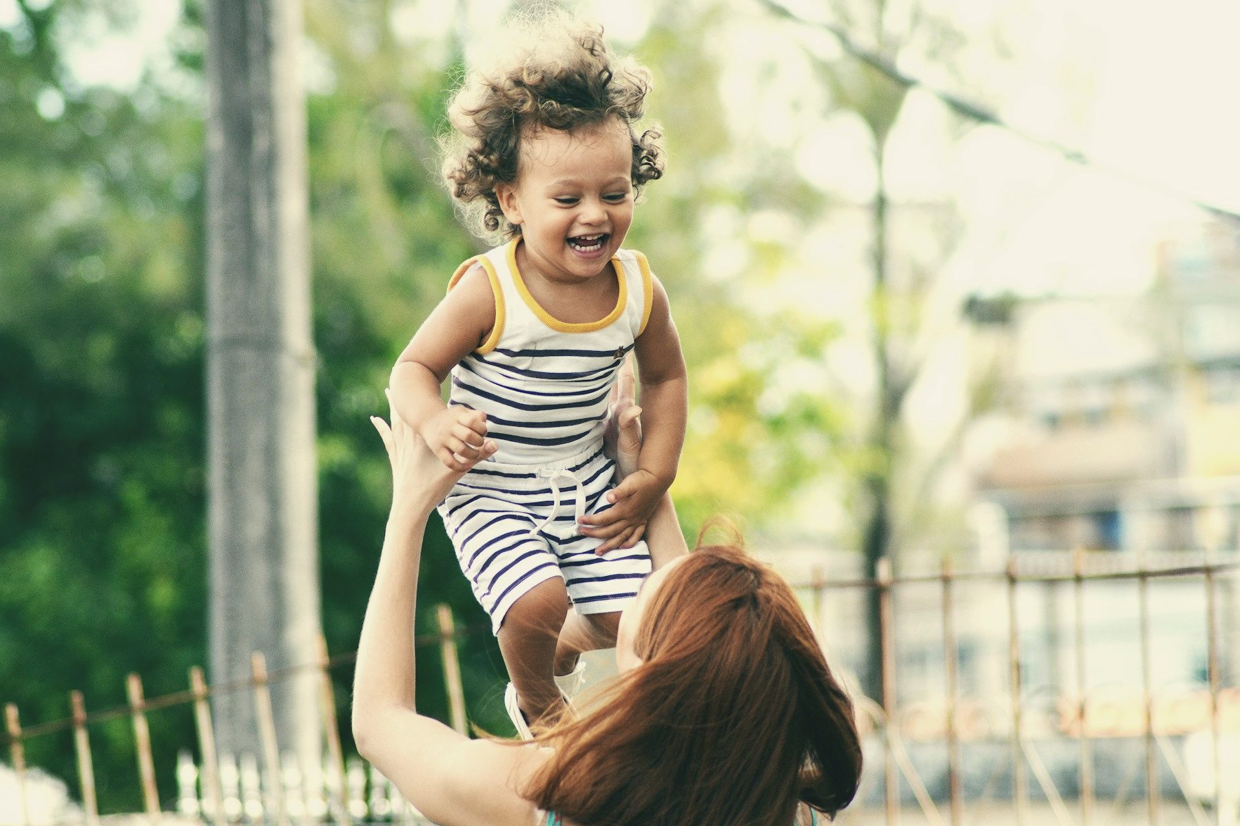 A mother lifting her laughing toddler into the air outdoors