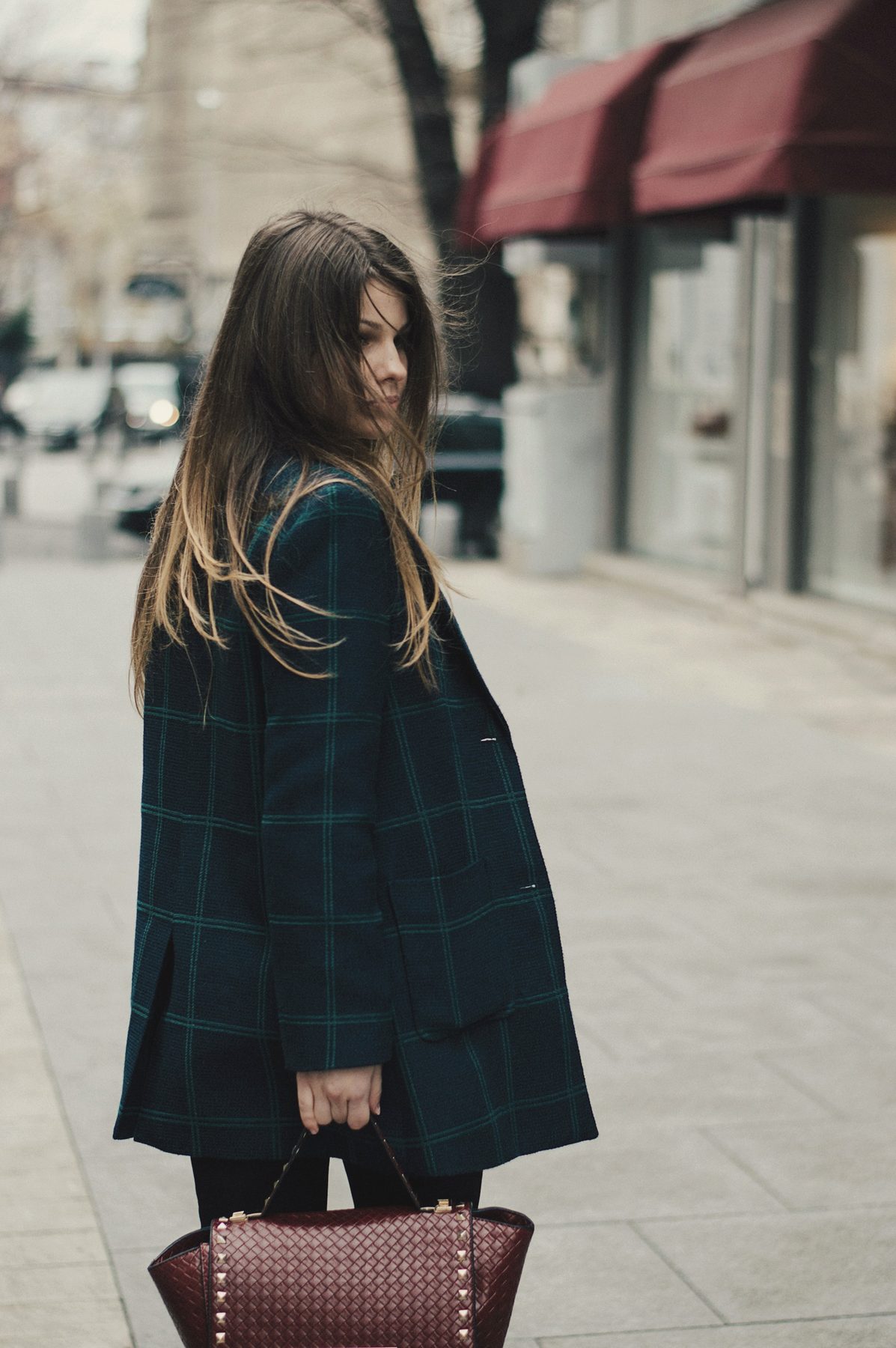 A woman in a long check coat looking back over her shoulder on a quiet street