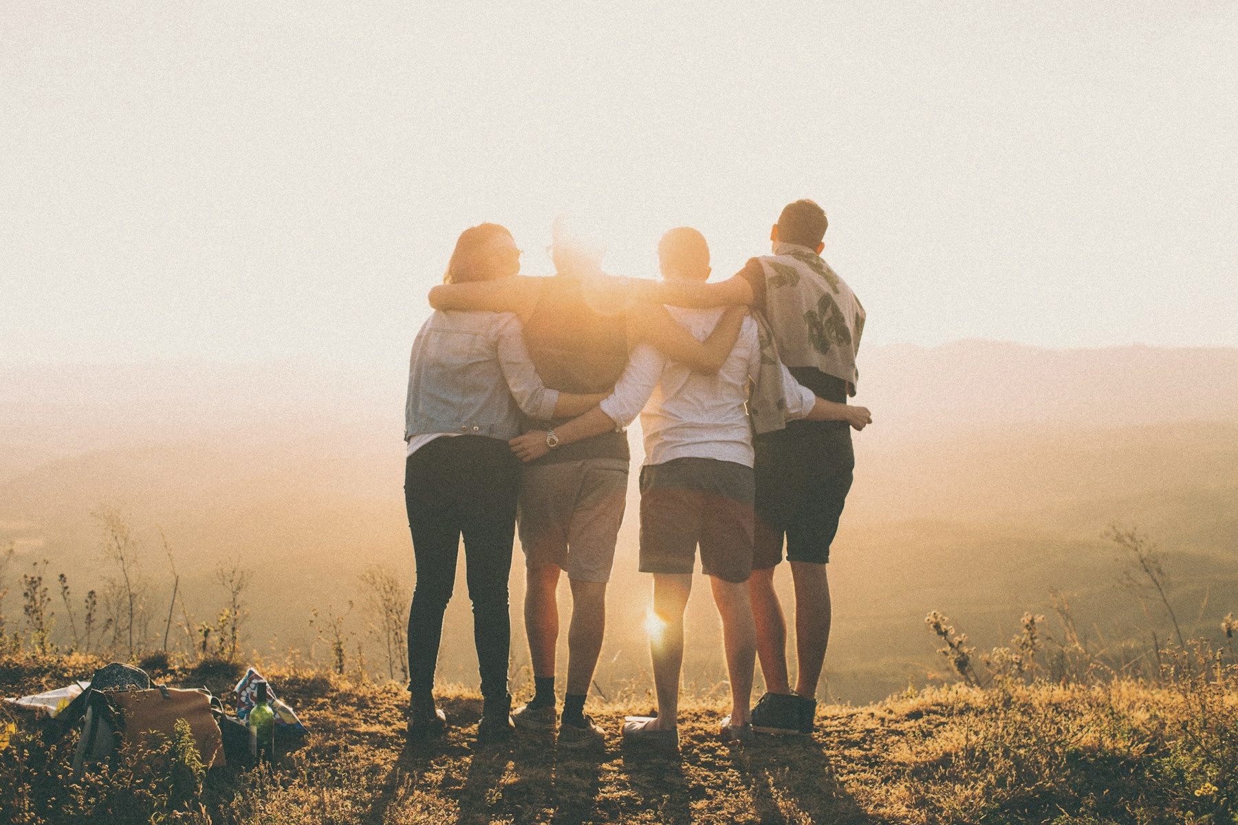 Four friends arm in arm on a hillside, watching the sun go down