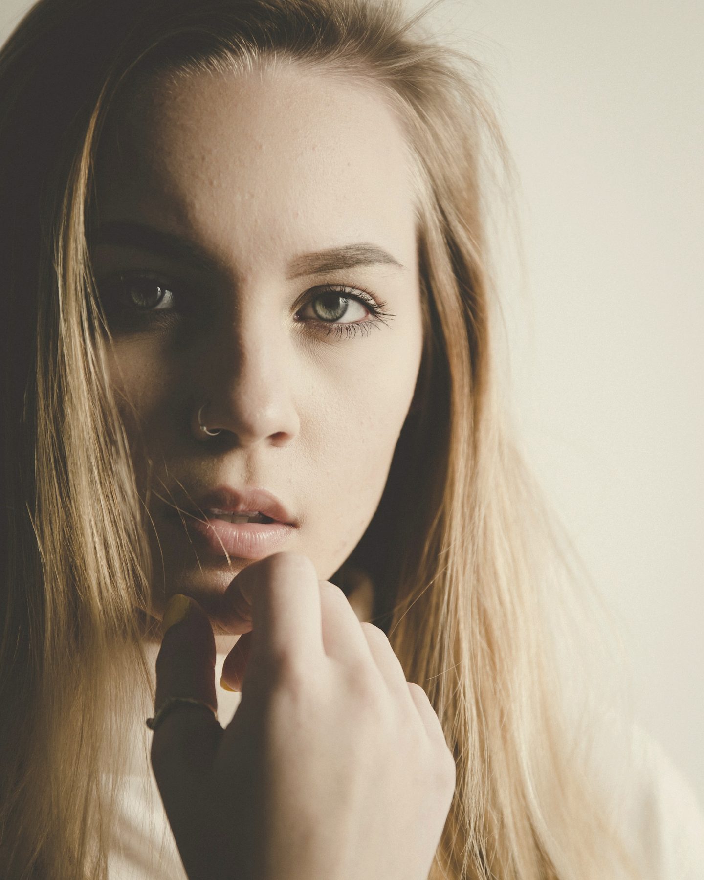 A close portrait of a woman with fair hair, her hand at her chin