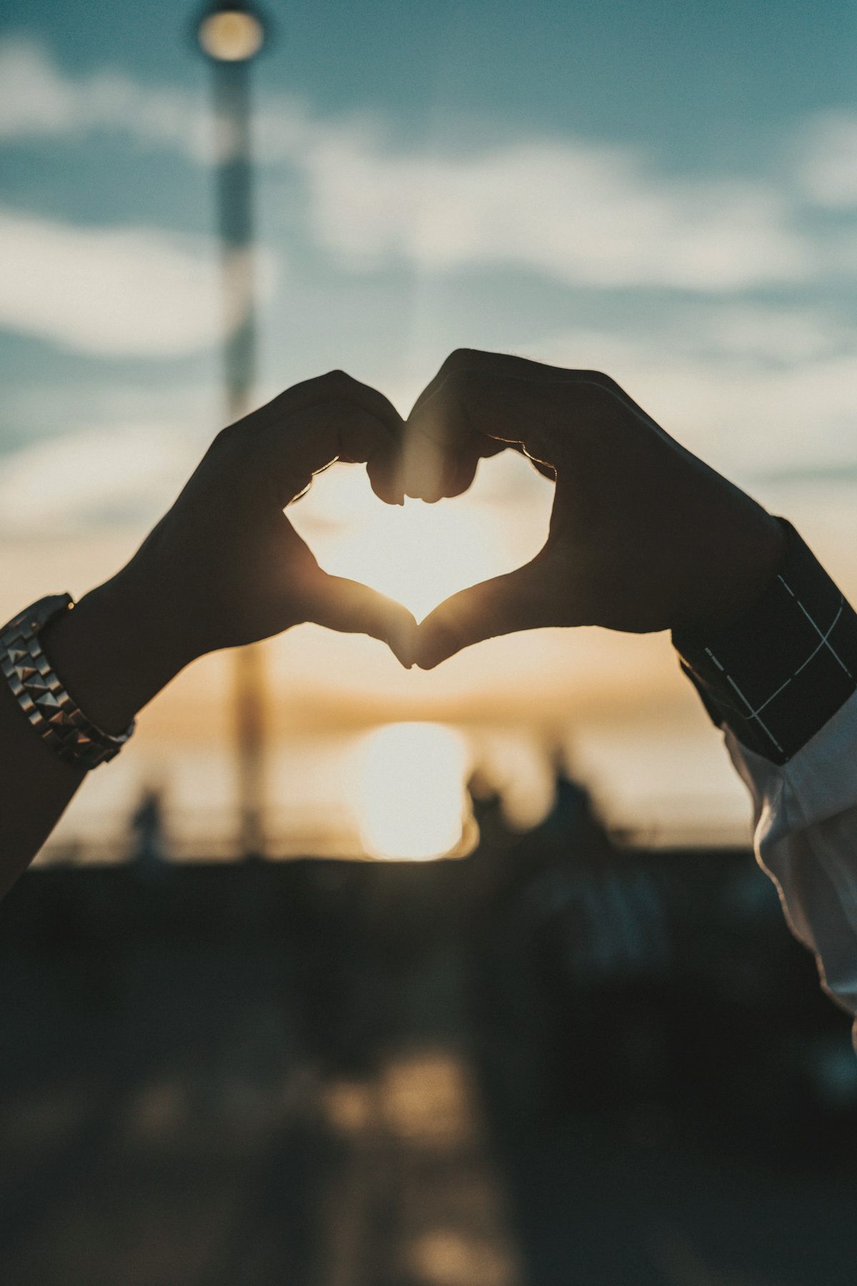 Two hands forming a heart shape against the setting sun