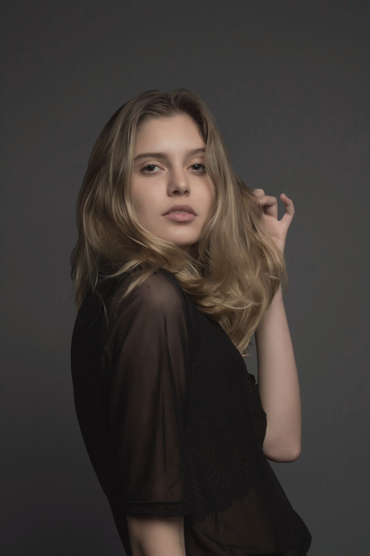 A woman in a sheer black top against a dark backdrop