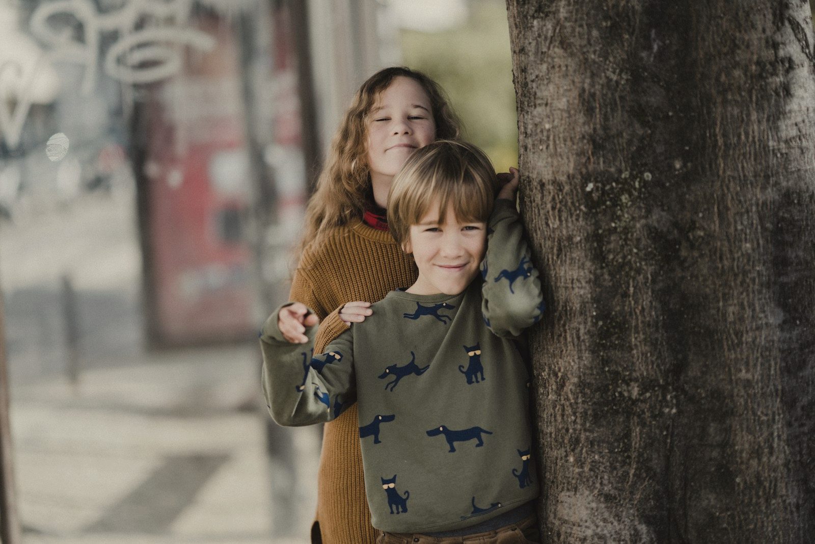 Two children leaning against a tree, one behind the other