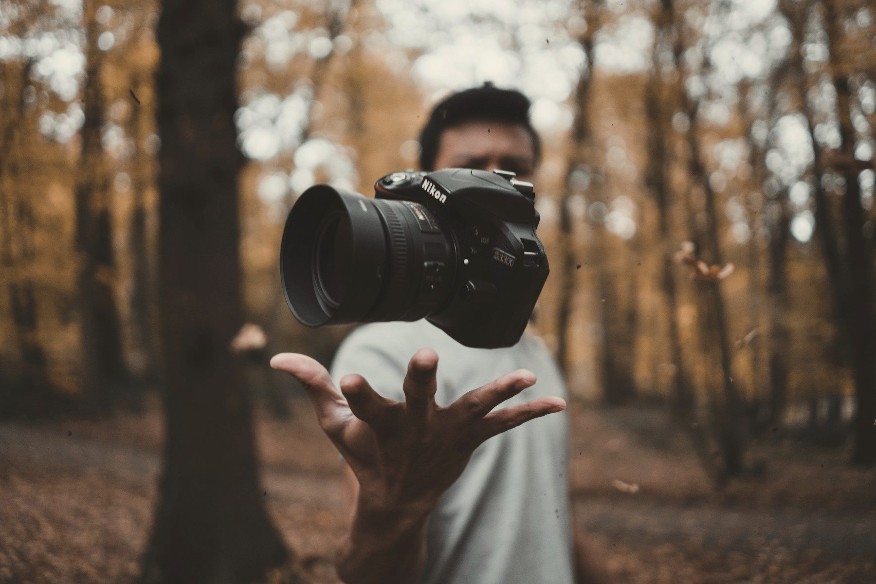 A photographer holding a camera towards the lens among autumn trees