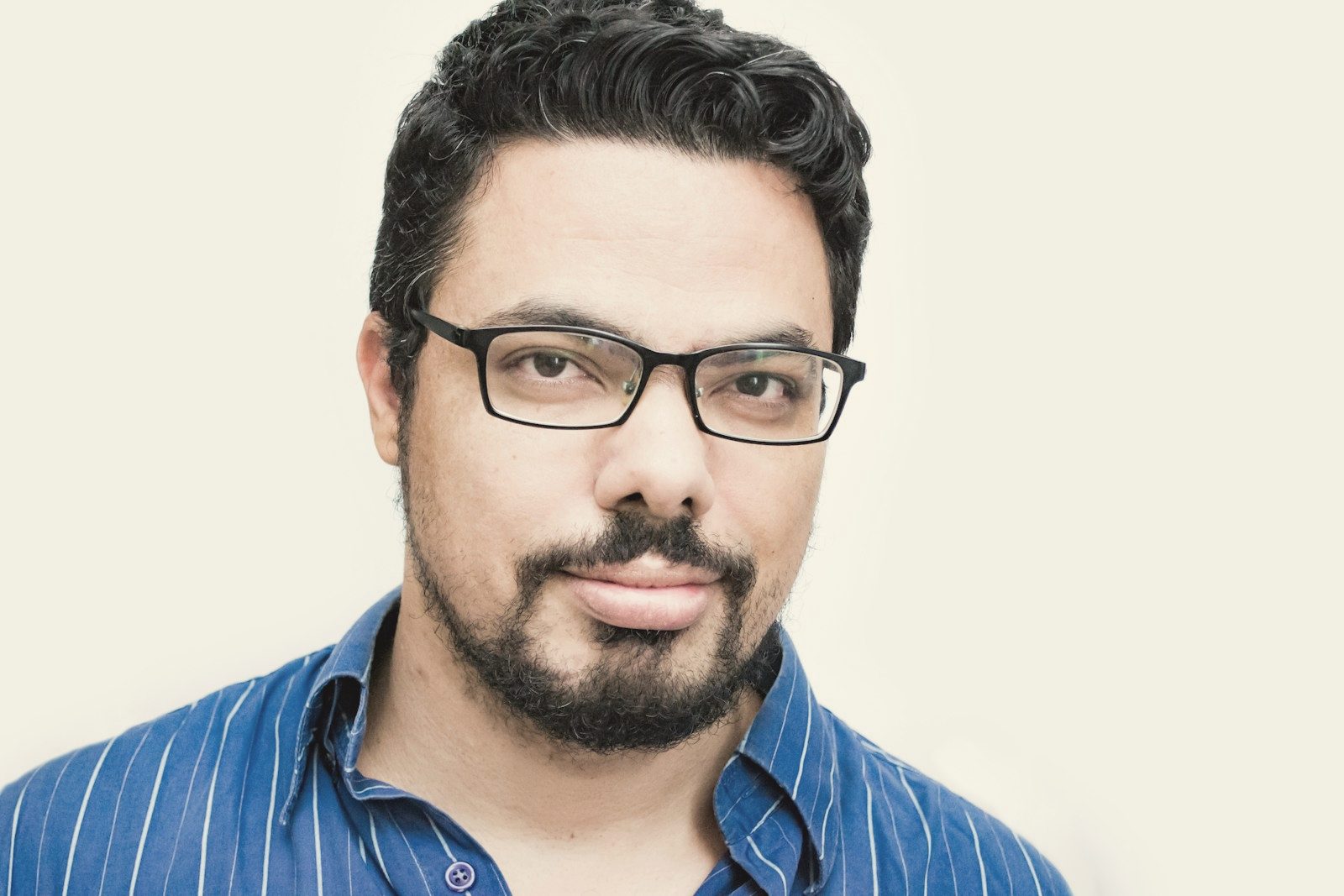 A man in glasses and a blue shirt against a plain wall
