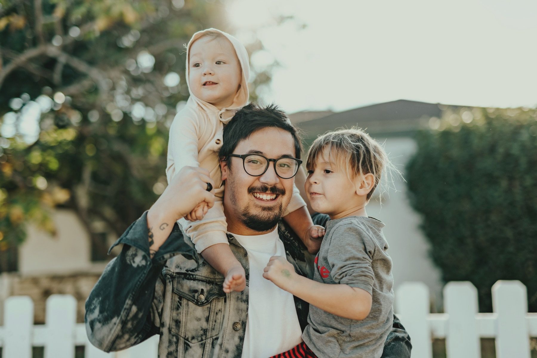 A father carrying two small children outside their home